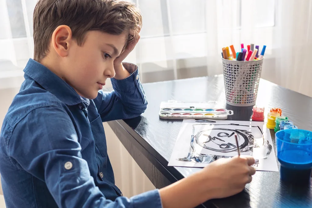 A sad young boy paints only in black, ignoring other colors, symbolizing childhood depression, stress, and emotional challenges. Concept of autism, mental health, art therapy
