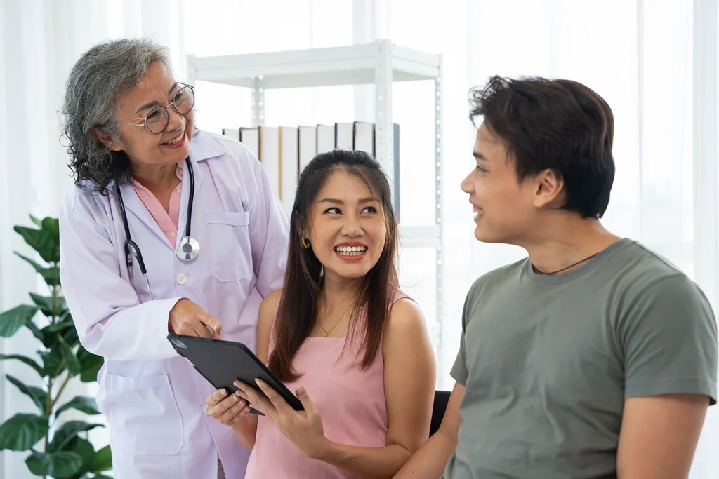 Senior female obstetrician consulting pregnant woman and her husband in medical clinic planning pregnancy.