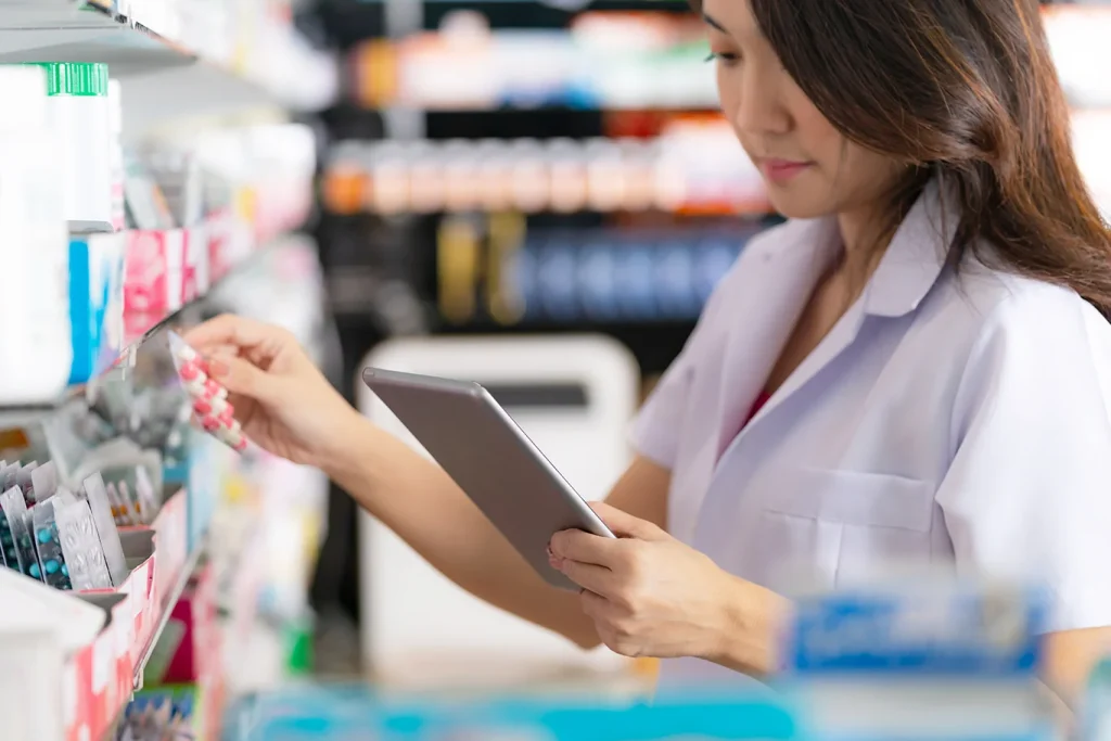 Female pharmacist taking a medicine from the shelf and uses digital tablet in the pharmacy