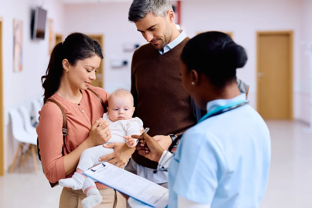 Parents with baby daughter talking to nurse in hallway of medical clinic.