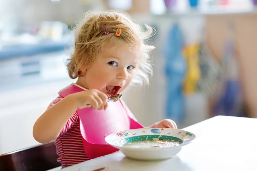 Adorable baby girl eating from spoon vegetable noodle soup